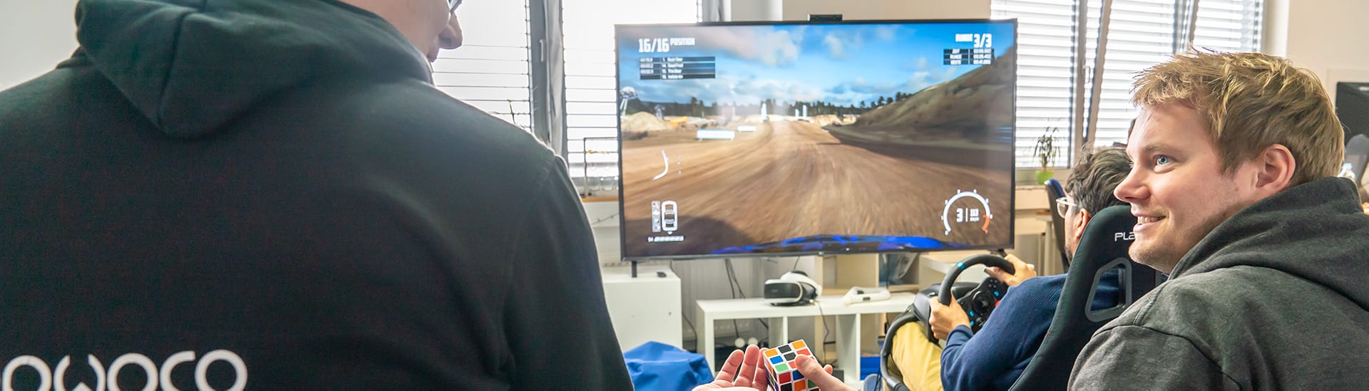 img_hero_karriere_mobile Mitarbeiter spielen ein Videospiel und mit einem Rubix Cube